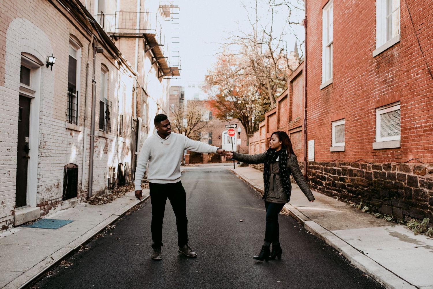 A playful couple holding hands and dancing in an urban alleyway between brick buildings.
