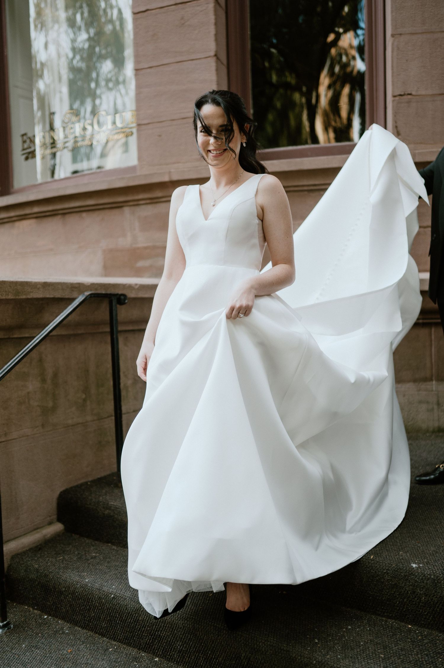 Flowing white wedding dress moves dramatically on stone steps of historic building.