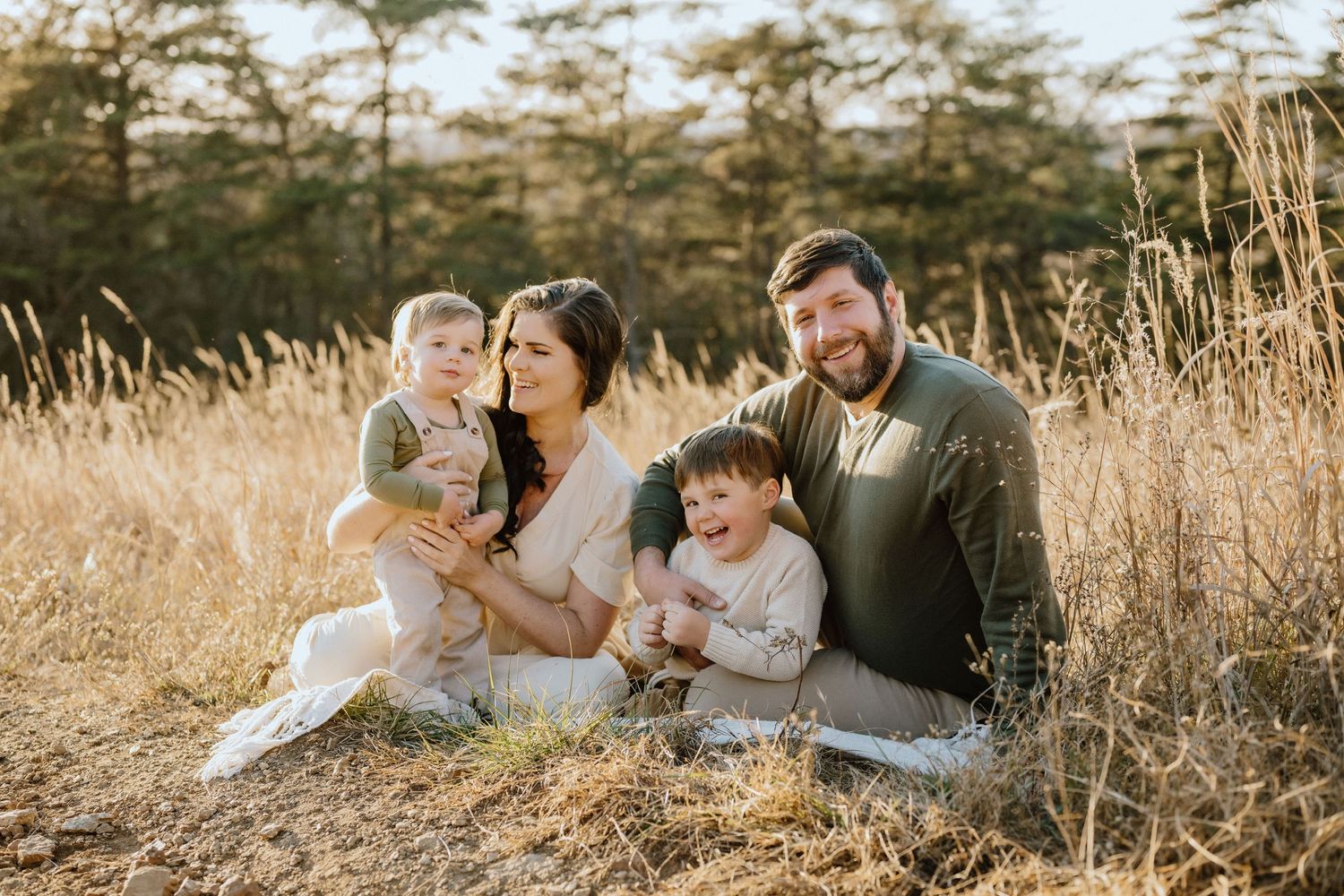 Family of four sitting together on a blanket in a sunlit meadow.