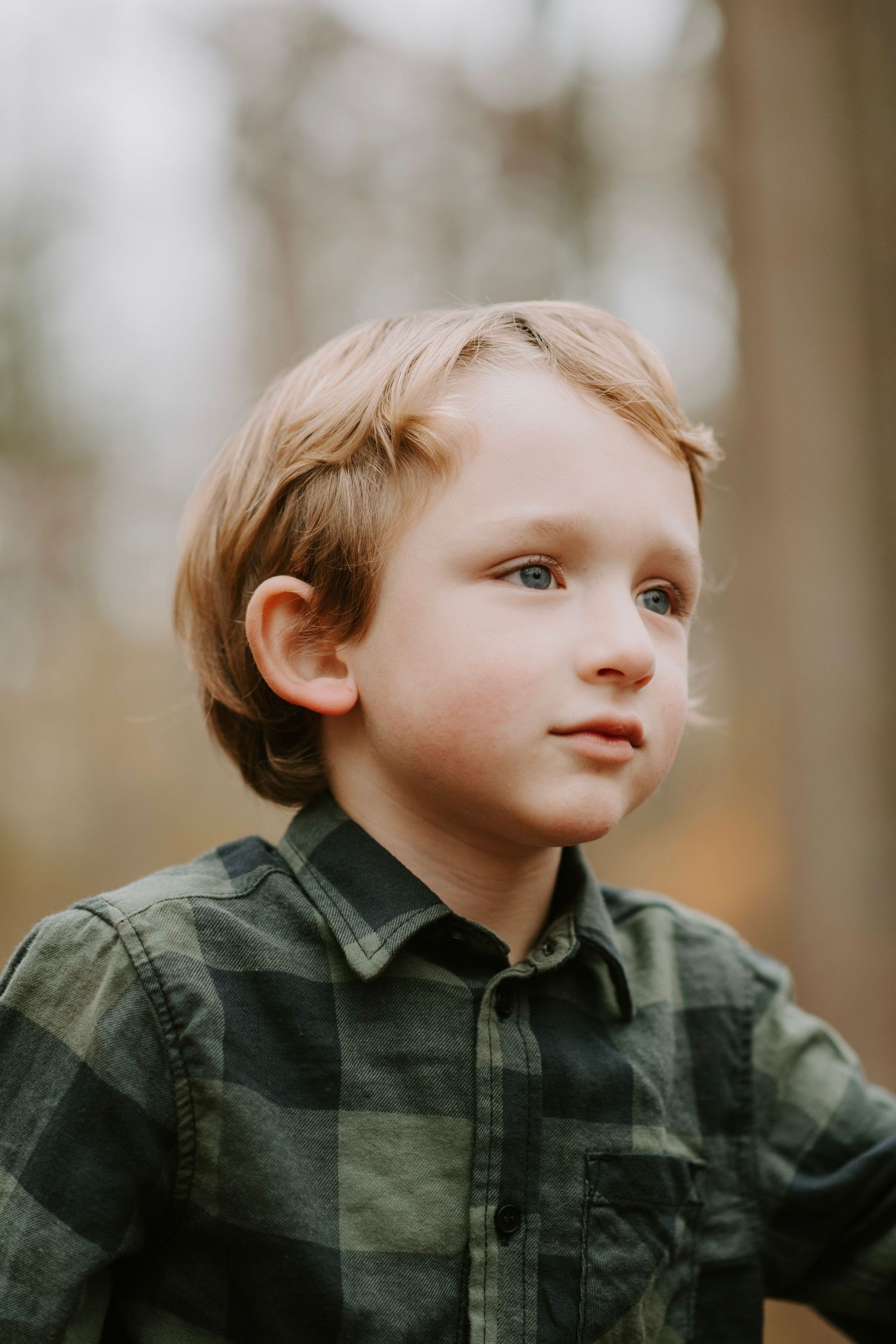 Close up portrait of child wearing plaid shirt in autumn woods.
