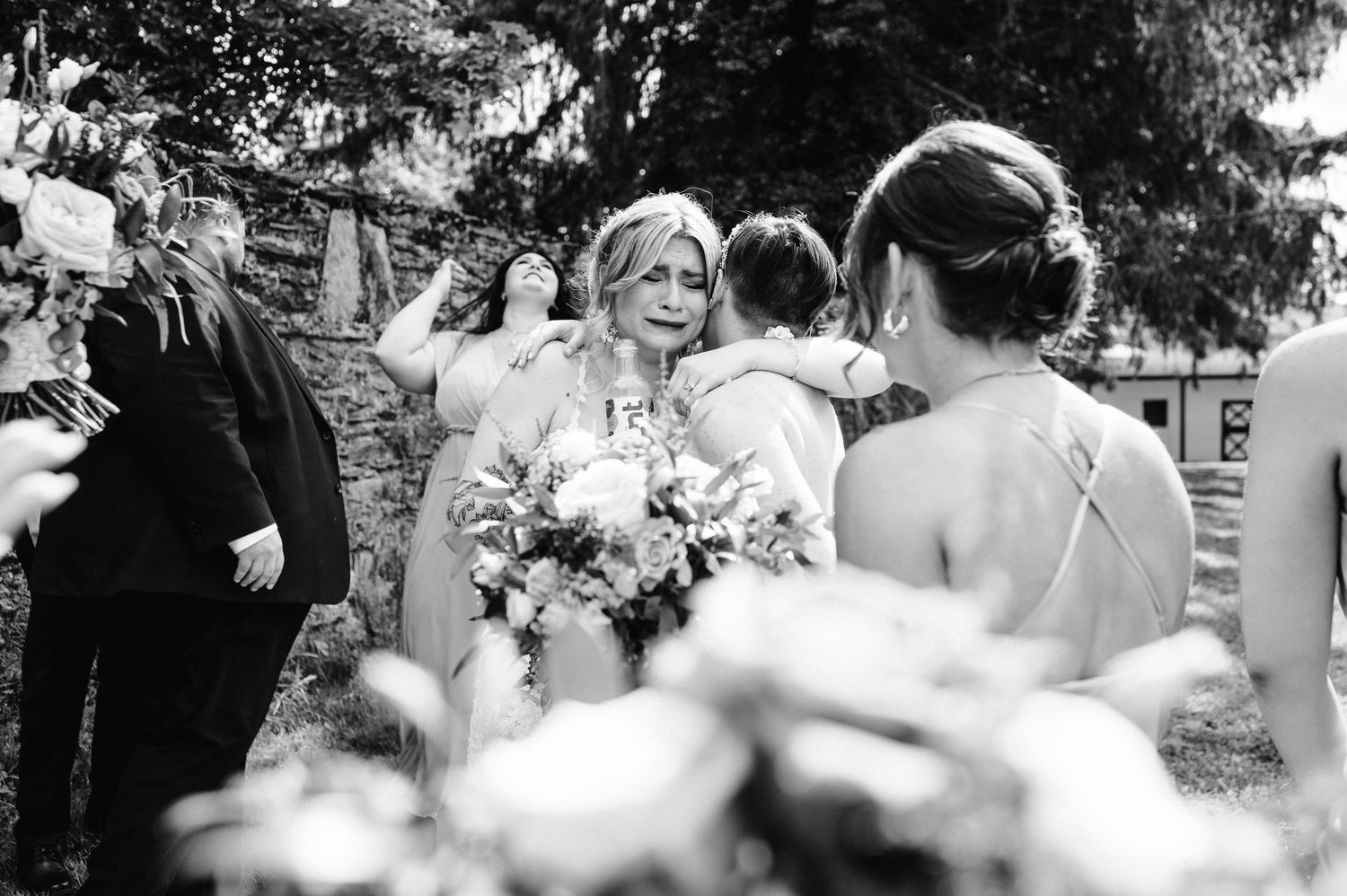 Black and white photo of bride with bouquet surrounded by wedding party outdoors.