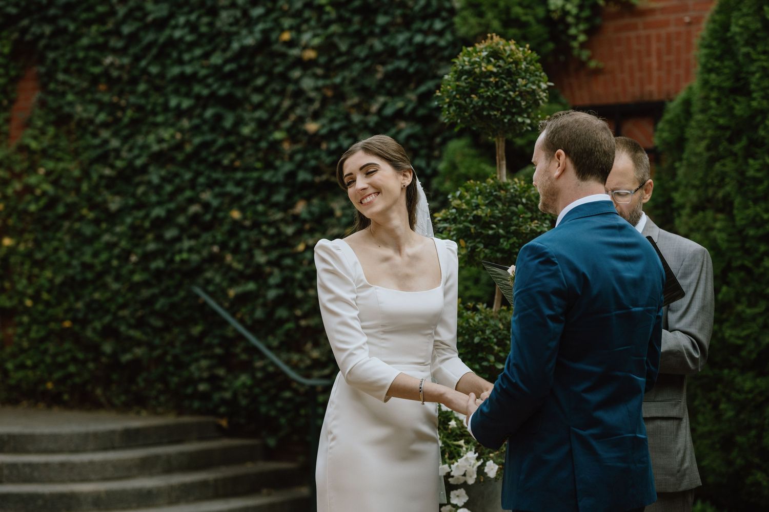 An intimate moment during a wedding ceremony against an ivy-covered brick wall backdrop.