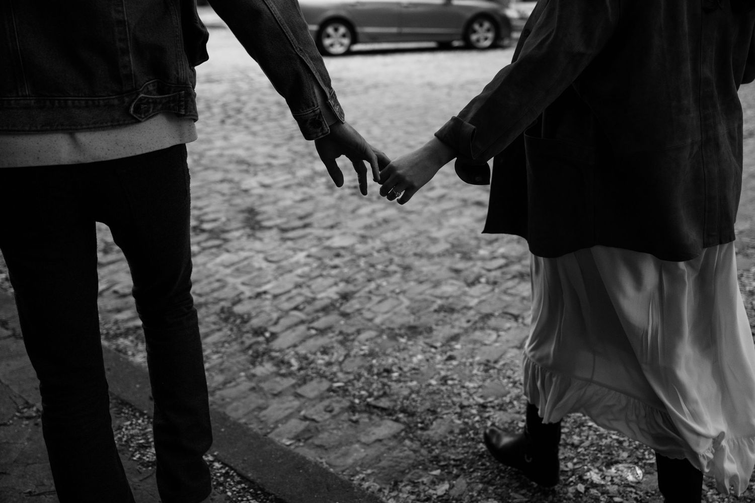 Black and white photo of a couple holding hands on a cobblestone street.