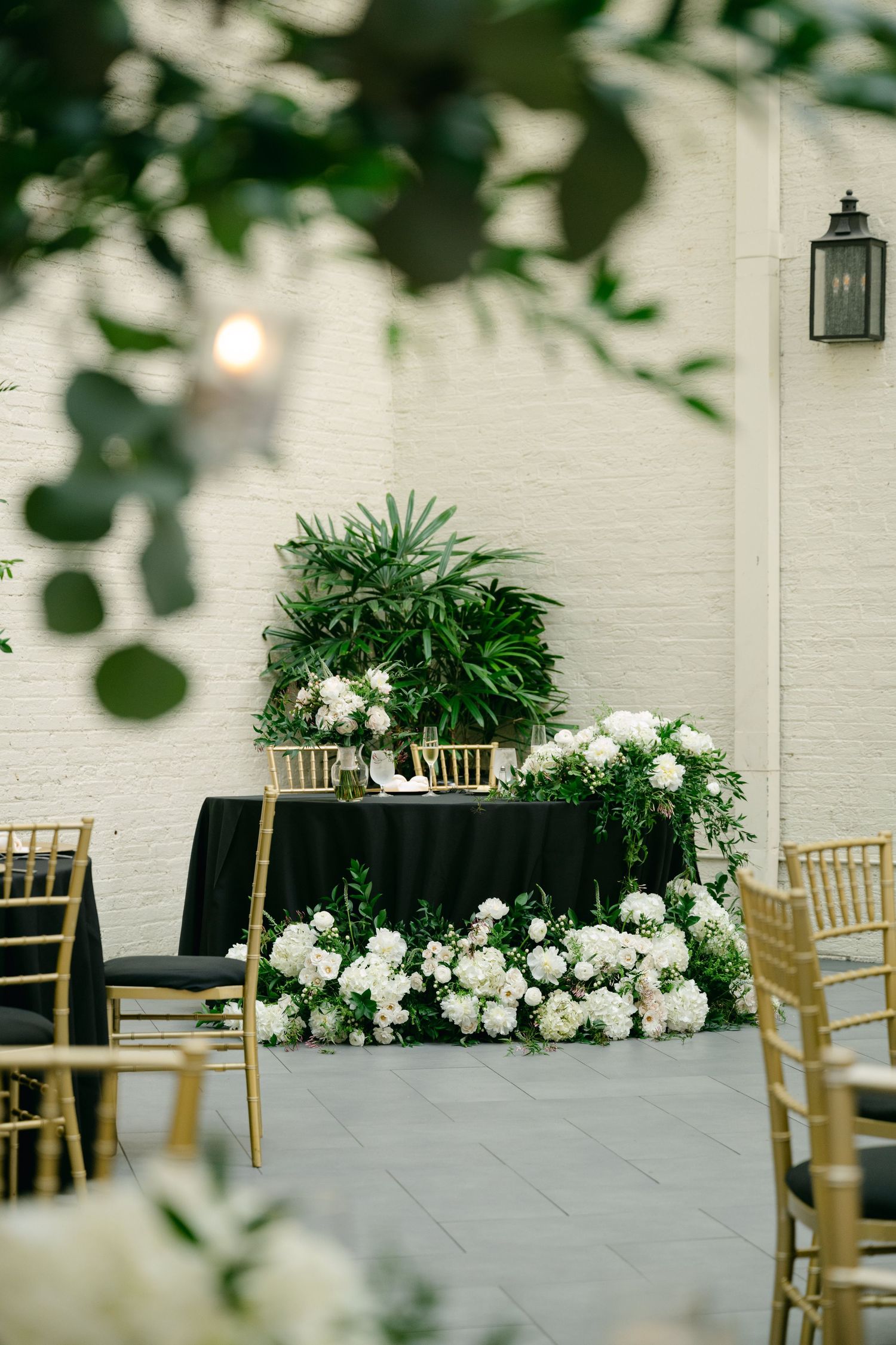 Modern wedding venue with white brick walls, gold chairs, and lush floral arrangements.