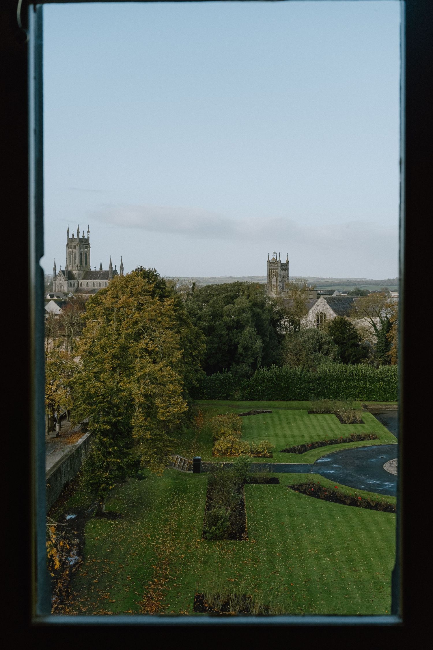 Cathedral towers rise above manicured gardens and autumn trees in a scenic landscape.