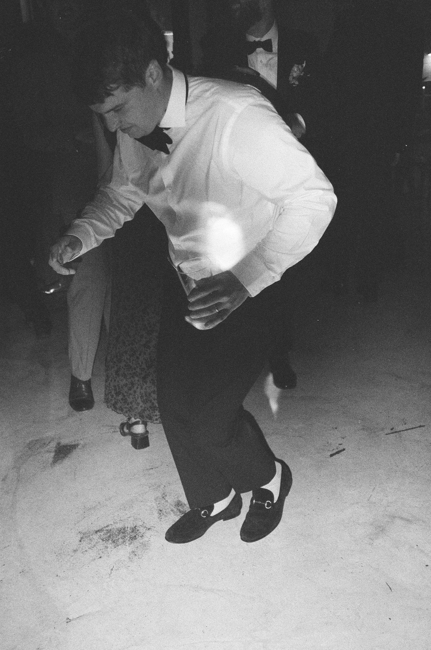 Black and white photo of someone performing an energetic dance move in formal attire.