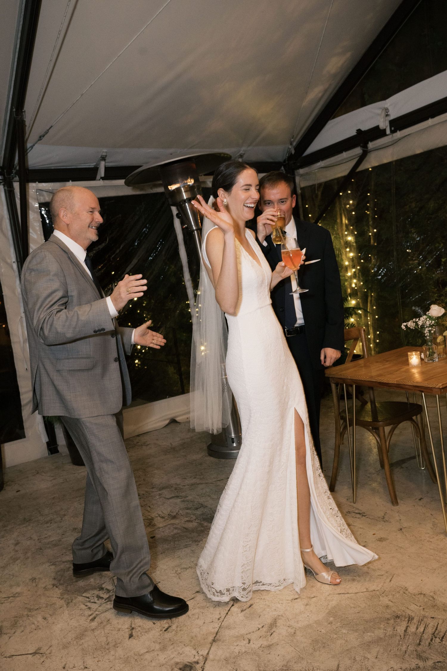 Wedding celebration under a white tent with guests enjoying drinks and conversation.