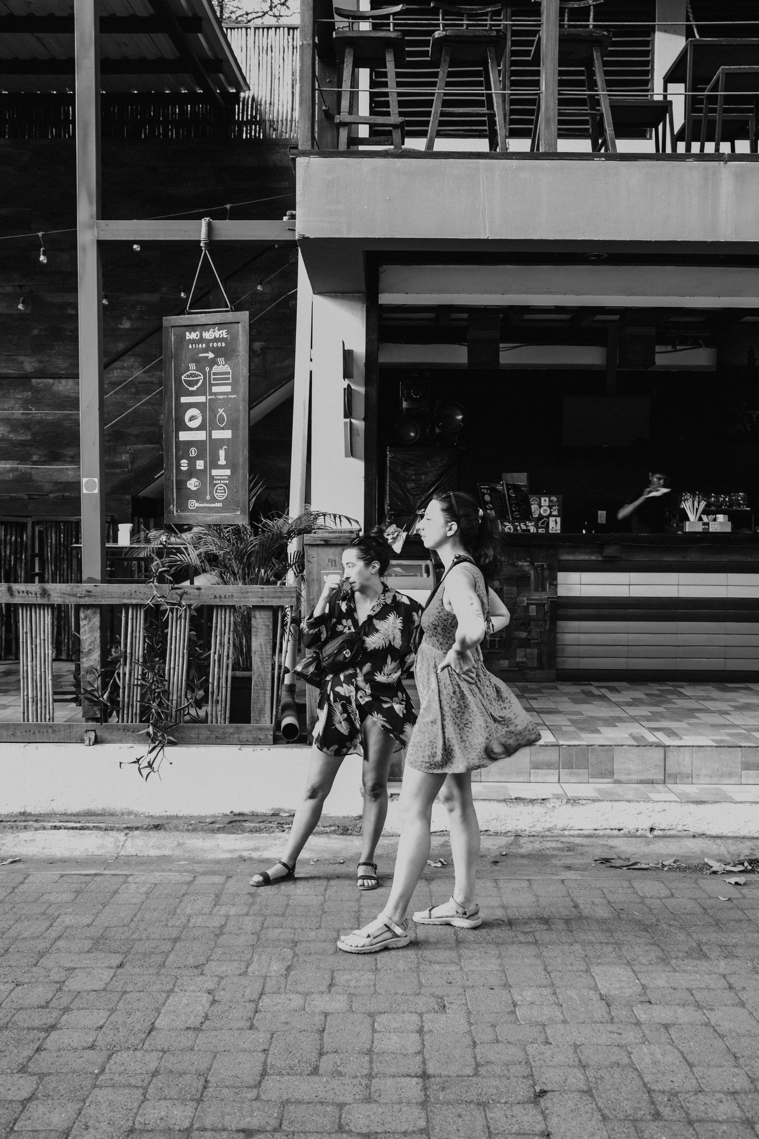 People exploring a brick-paved street near shops in a tropical setting.