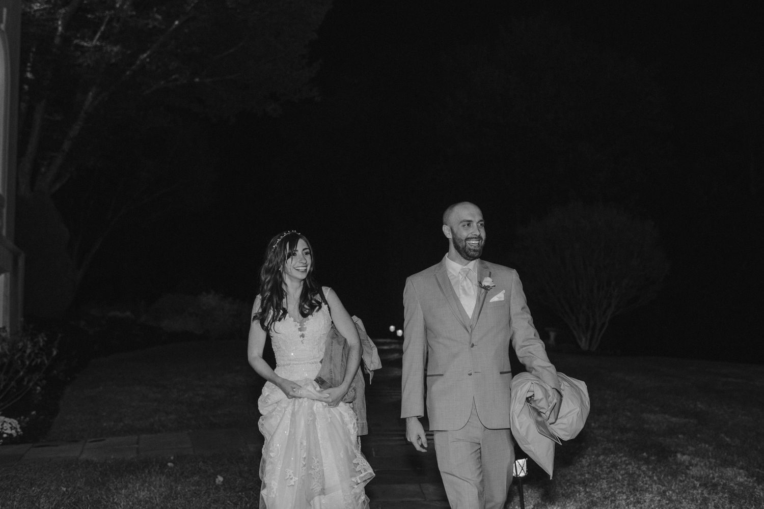 Black and white photo of newlyweds walking together on an outdoor path.