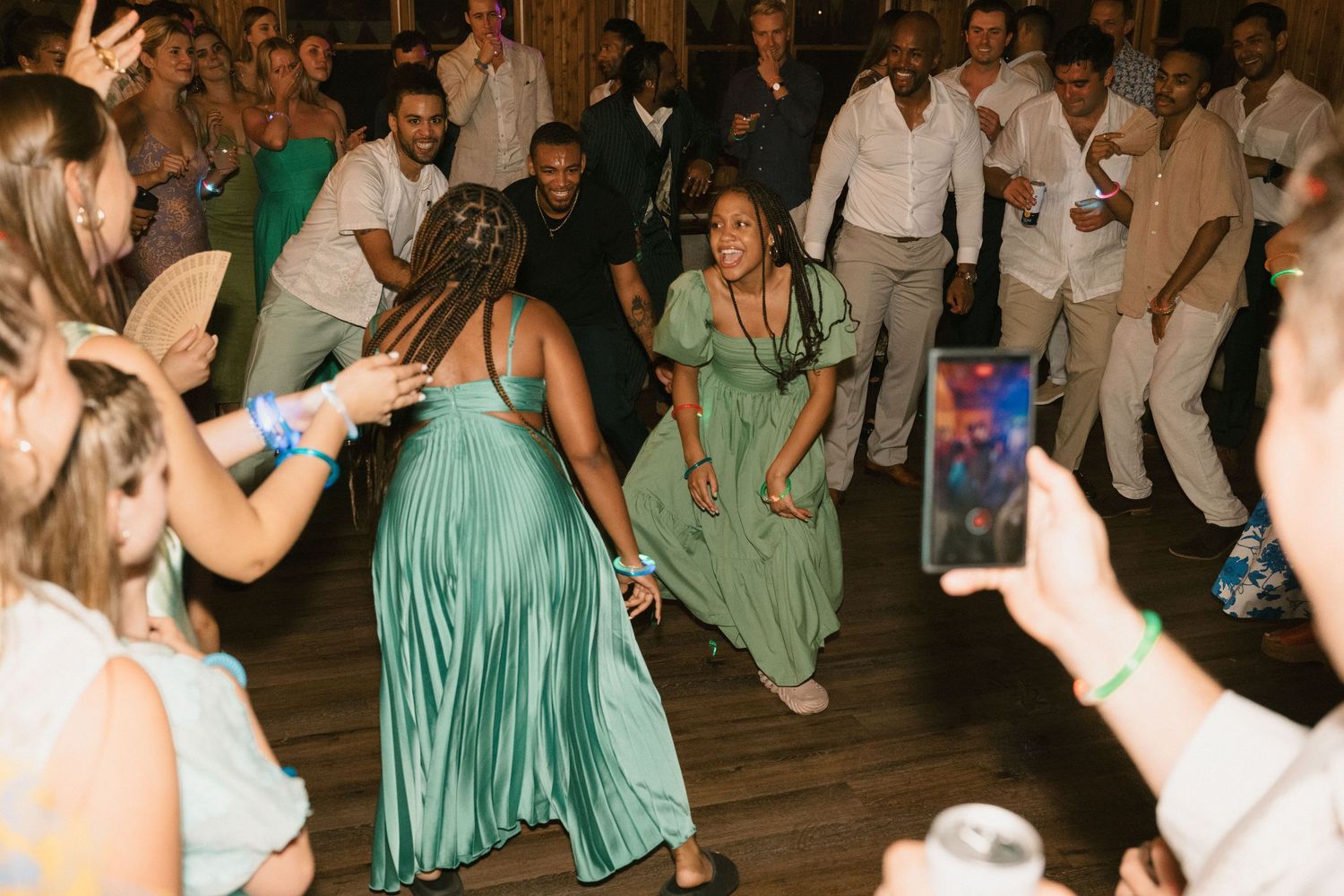 Party guests dancing in elegant attire on wooden dance floor with a seafoam green dress in focus.