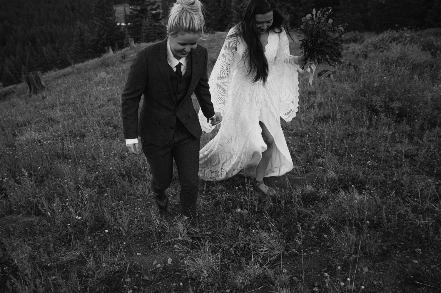 A couple walking together through mountain wildflowers in formal attire.