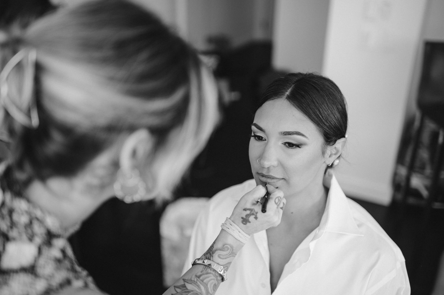 Close-up of makeup application showing tattooed hand and white robe.