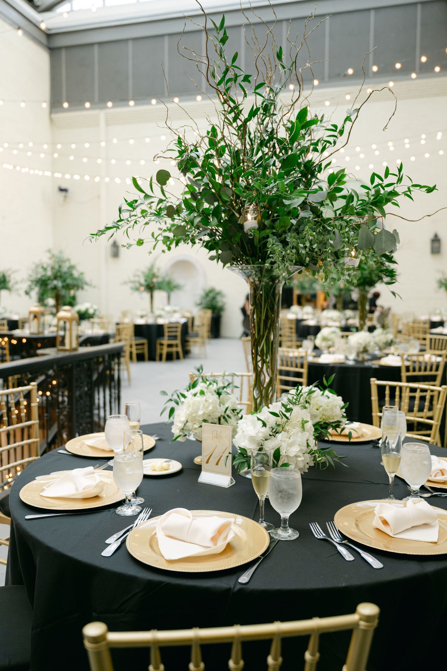 Elegant wedding reception table with tall greenery centerpiece, gold chargers, and black linens at a Baltimore engineers club wedding