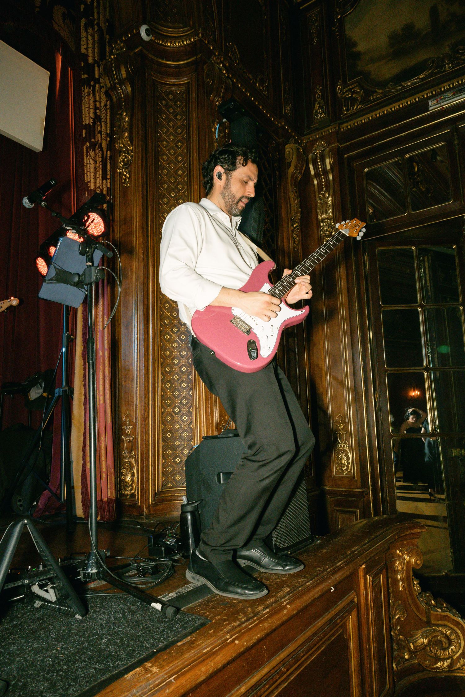 Guitar player performing on ornate wooden stage with red electric guitar.