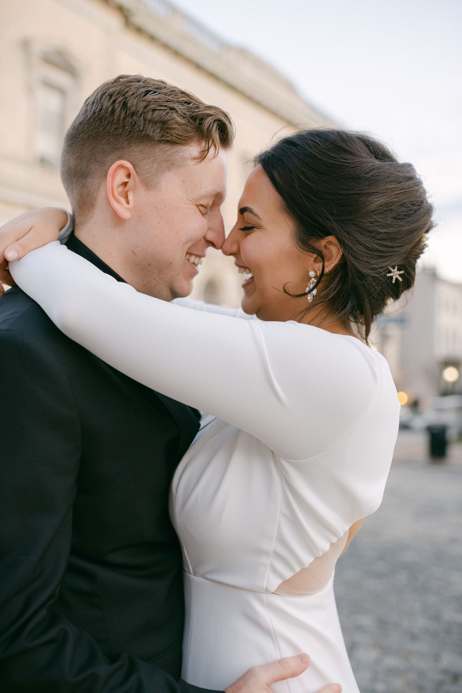 Intimate wedding portrait of couple embracing in formal attire against urban backdrop.