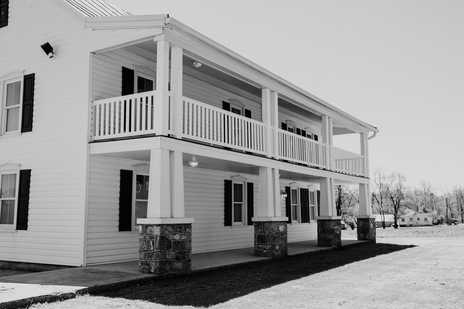 Classic white two-story farmhouse with wraparound porch and stone foundation details.