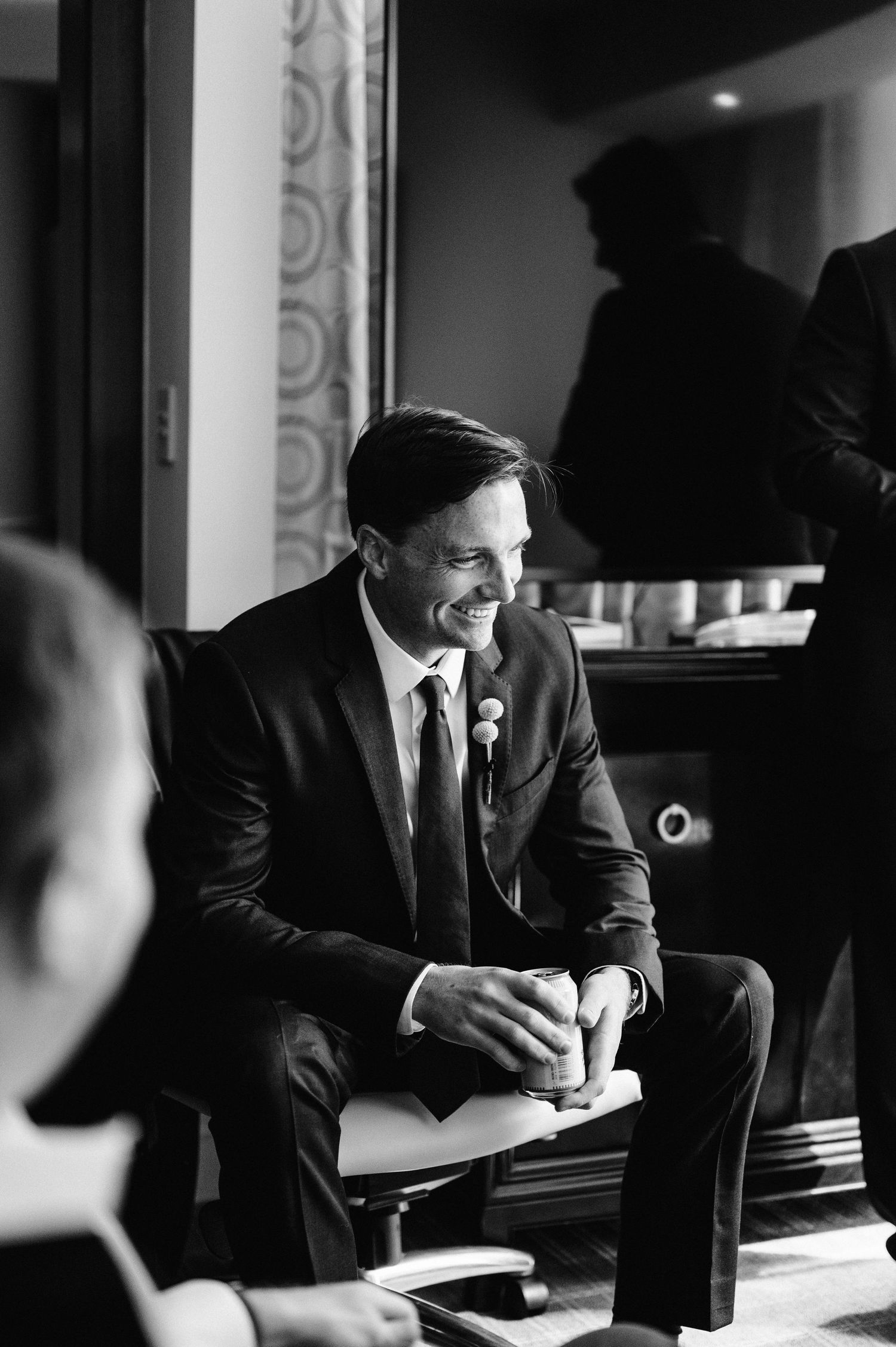 Black and white photo of groom sitting relaxed in formal attire.