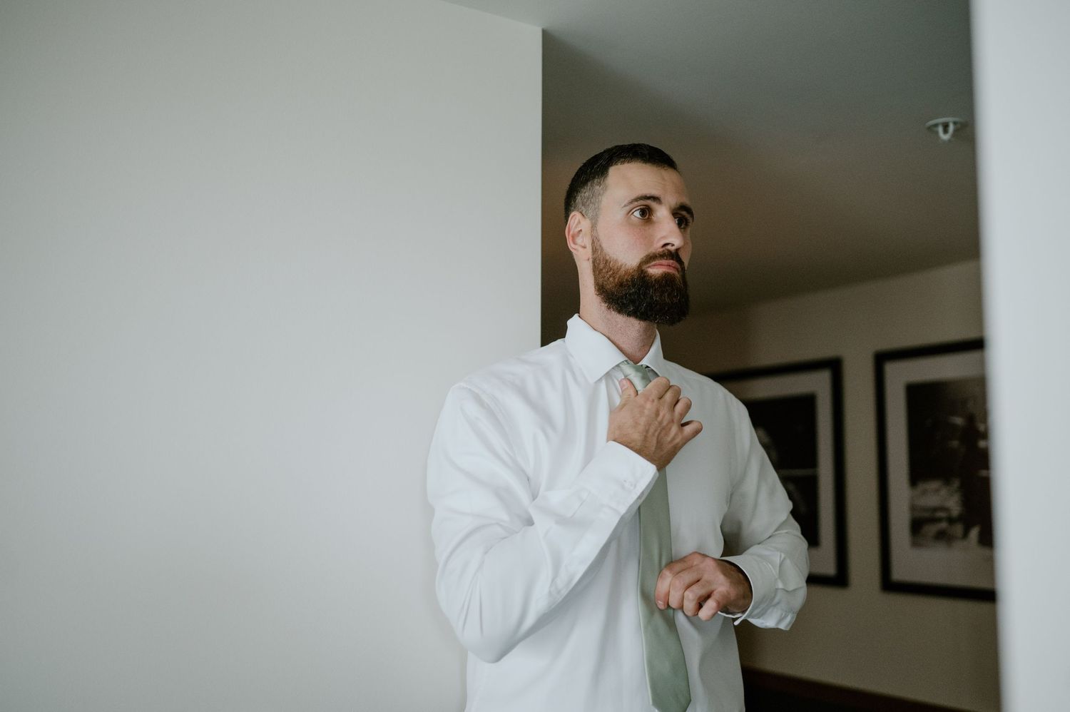 Person in white dress shirt adjusting tie while getting ready in modern interior.