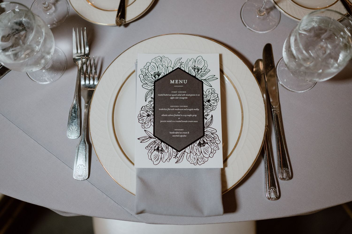 Elegant place setting with gold-rimmed white plate and ornate menu card featuring delicate floral design details.