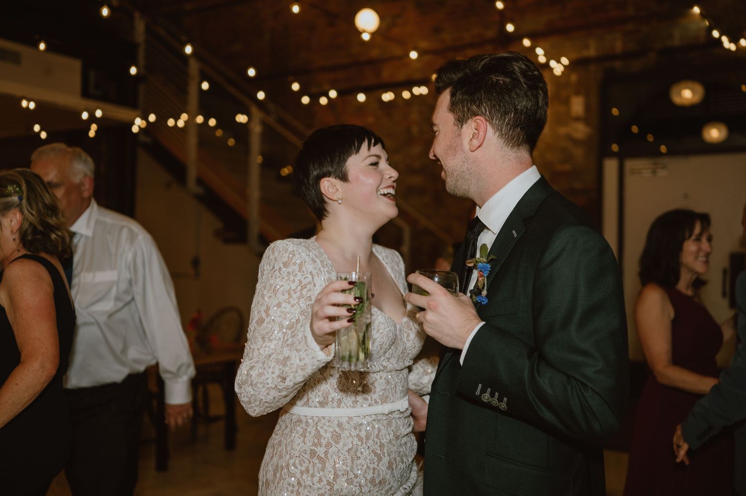 A candid moment of celebration at a wedding reception with string lights in the background.