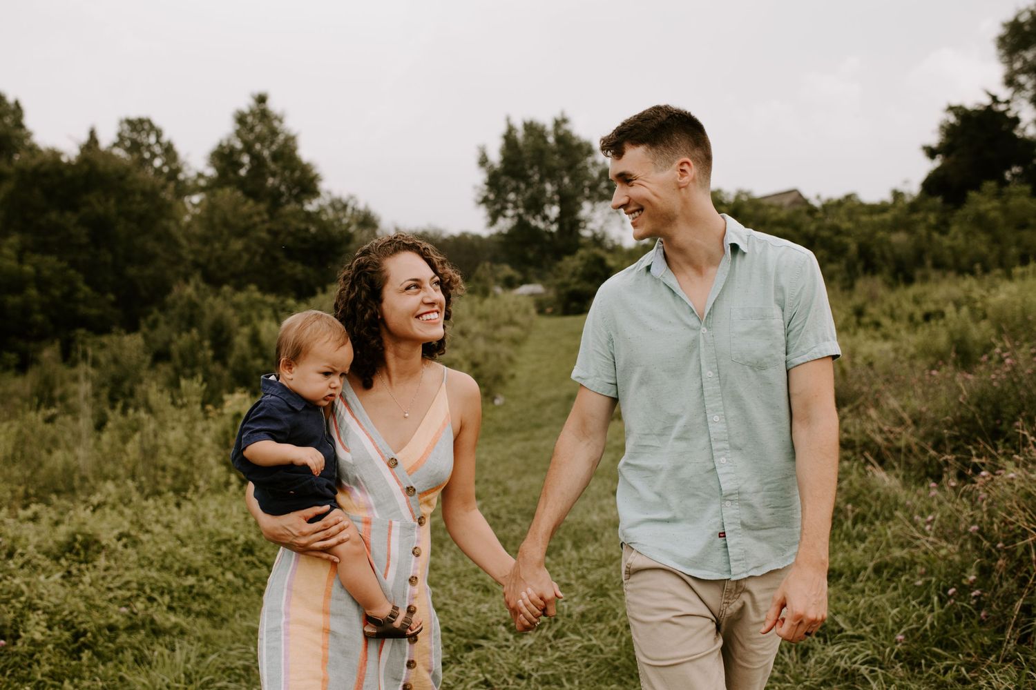 Family walking together through a green field on an overcast summer day.