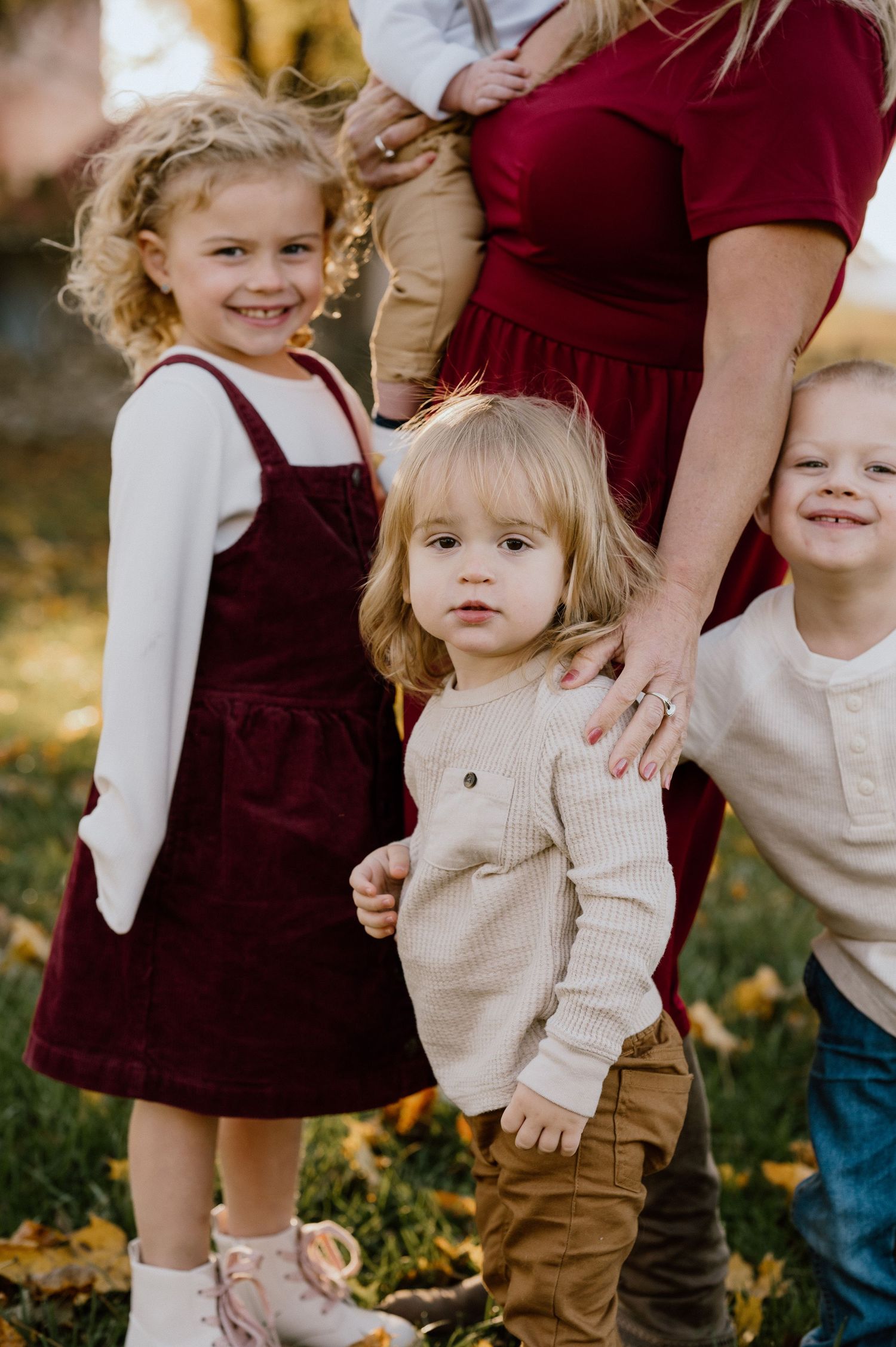 Children in autumn attire pose together among fallen leaves in a garden setting.
