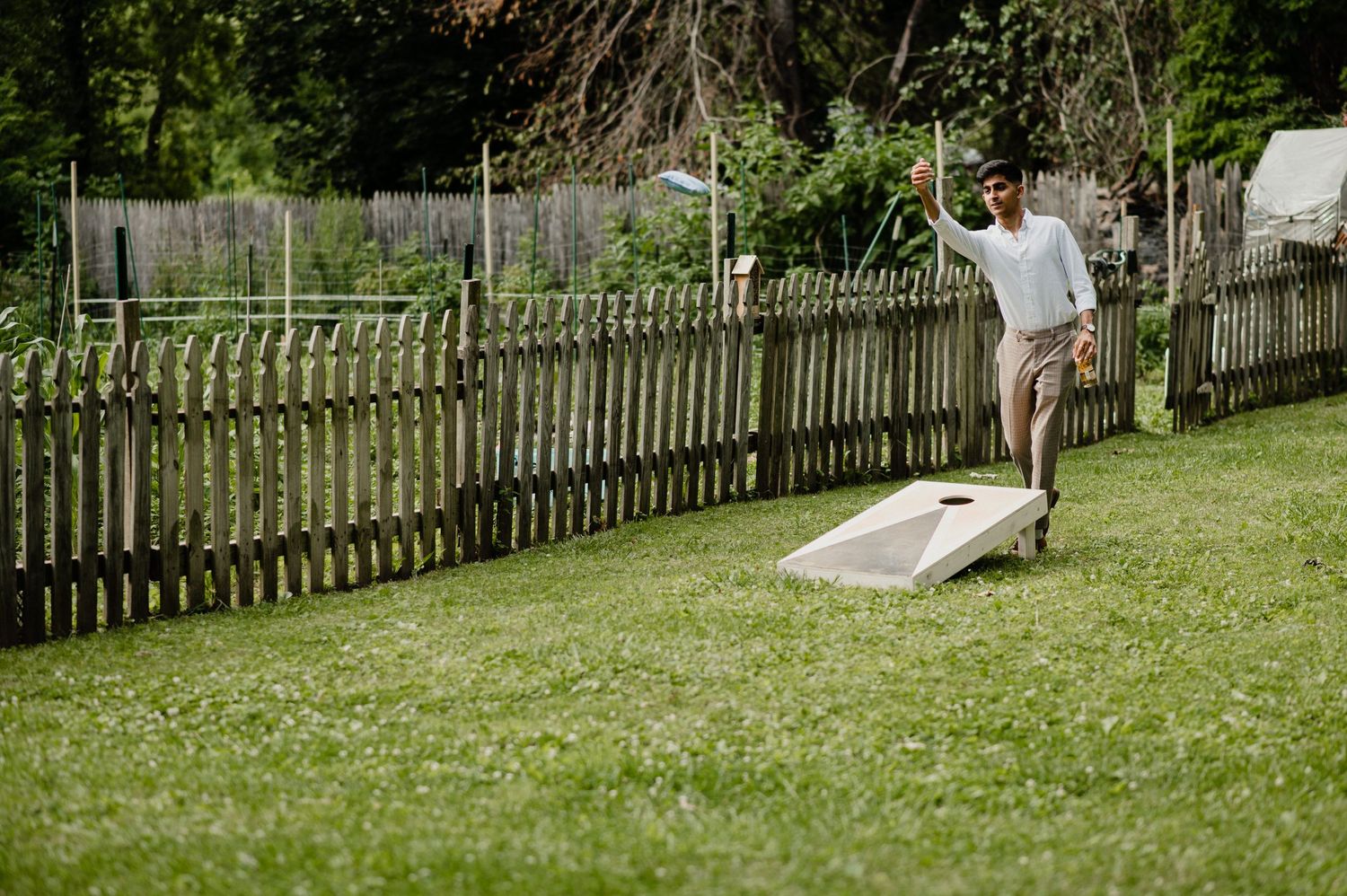 Someone playing cornhole in a backyard with a wooden fence on a sunny day.