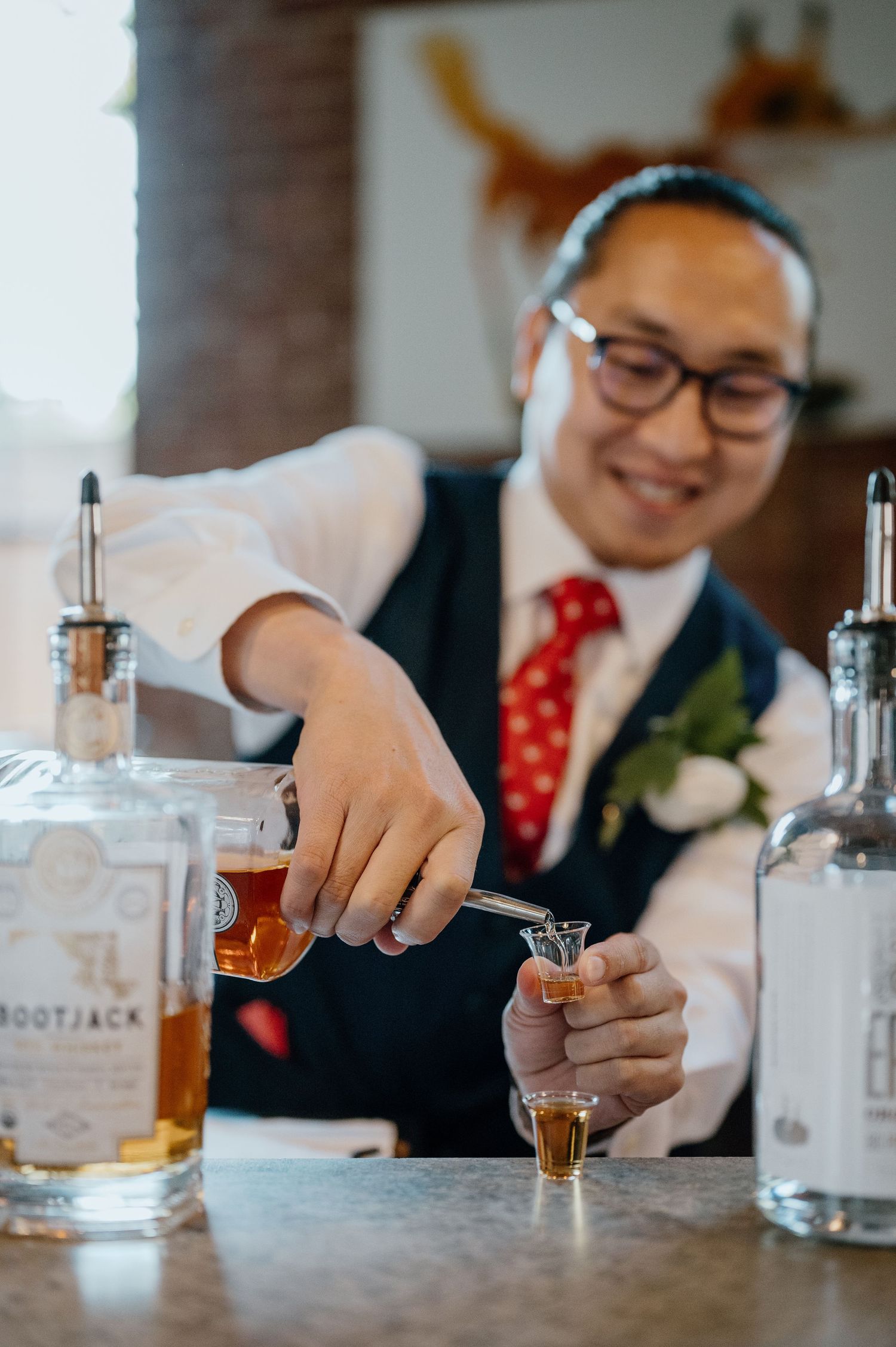Person in formalwear pouring drinks at a distillery bar counter.