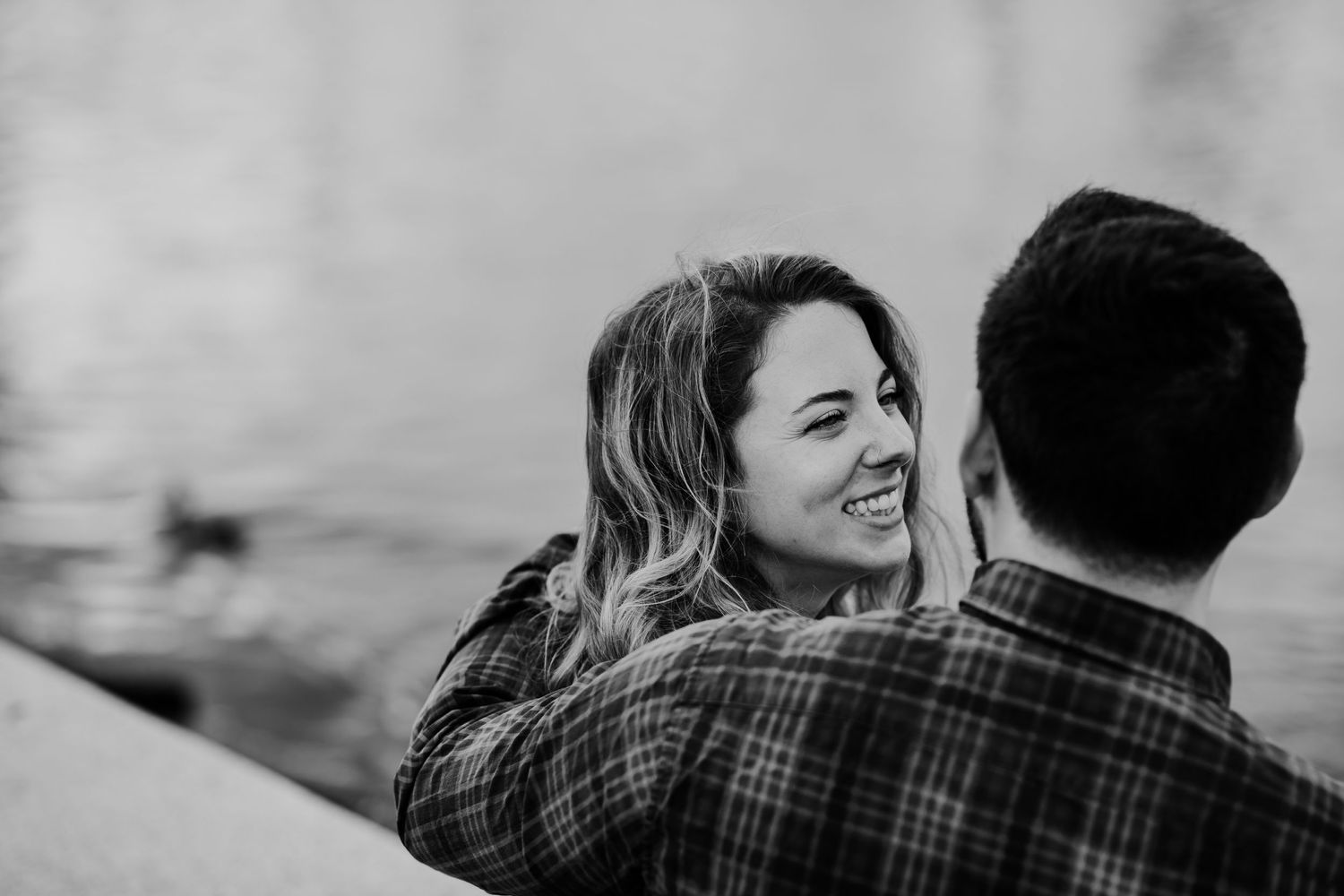 Black and white portrait of couple laughing together by the water.