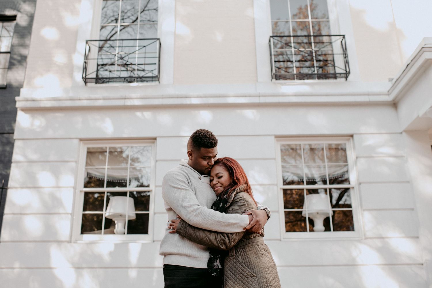 A romantic couple embracing outside a white building with elegant windows.