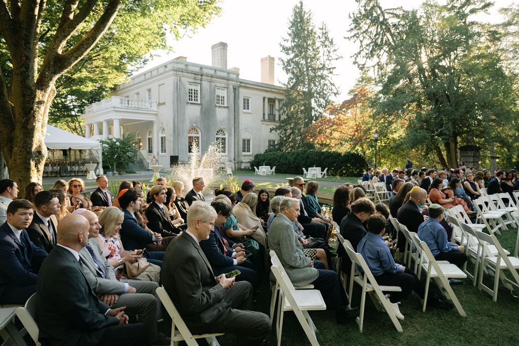 Wedding guests seated in white chairs on a lawn for an outdoor ceremony at Strong Mansion on Sugarloaf Mountain