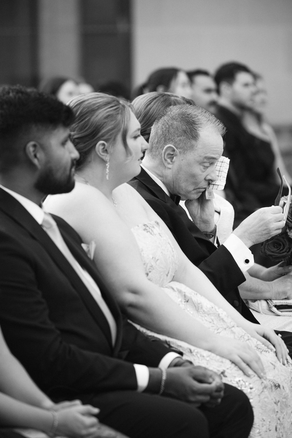 Black and white photo of wedding guests seated in formal attire during an emotional ceremony moment.