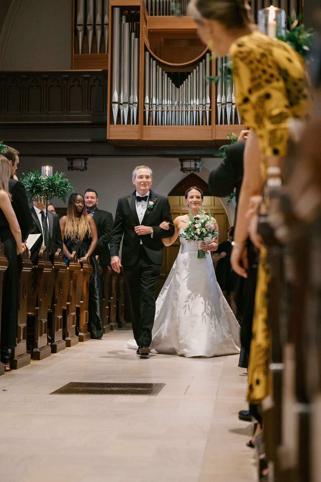 Wedding ceremony processional in a church with guests watching from wooden pews.