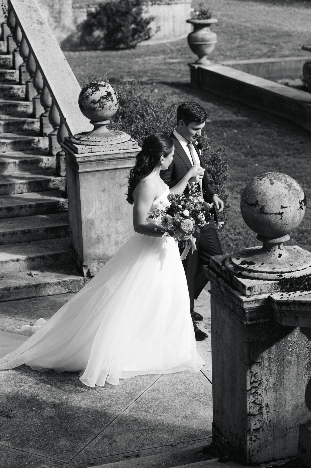 A person in a white wedding dress poses gracefully near ornate stone architecture in a black and white photo.