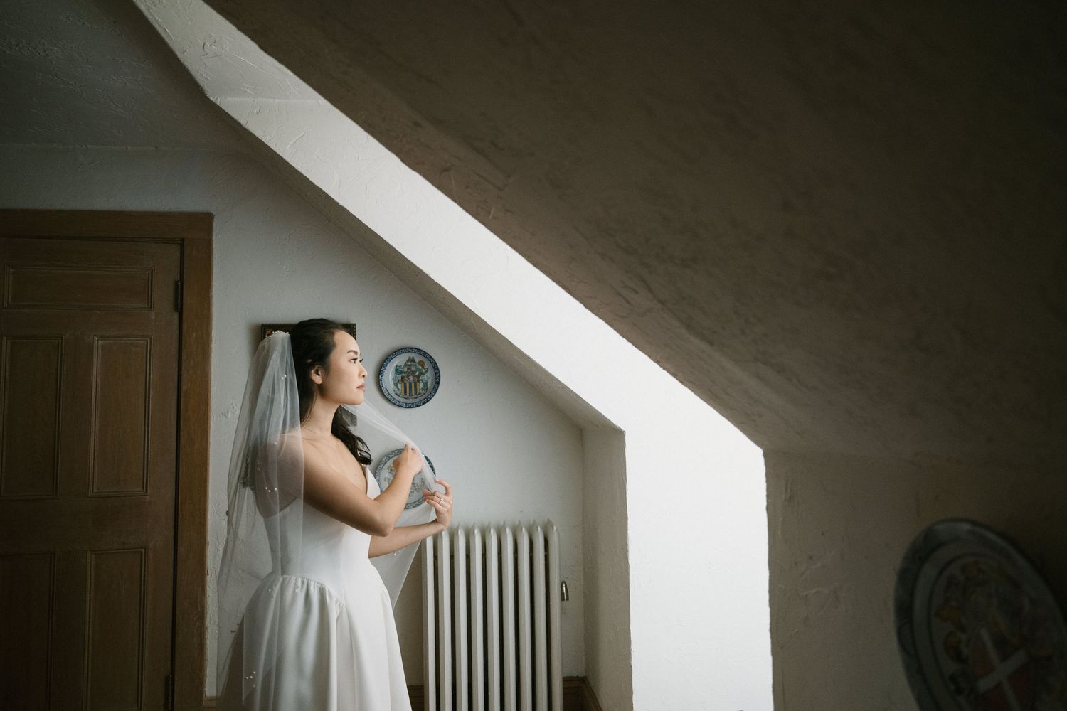 Dramatic lighting captures wedding dress silhouette in attic window.
