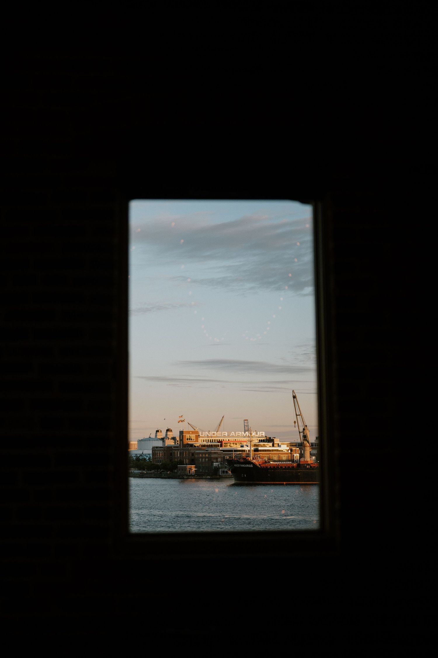 A scenic harbor view through a window frame during sunset showing industrial cargo equipment.