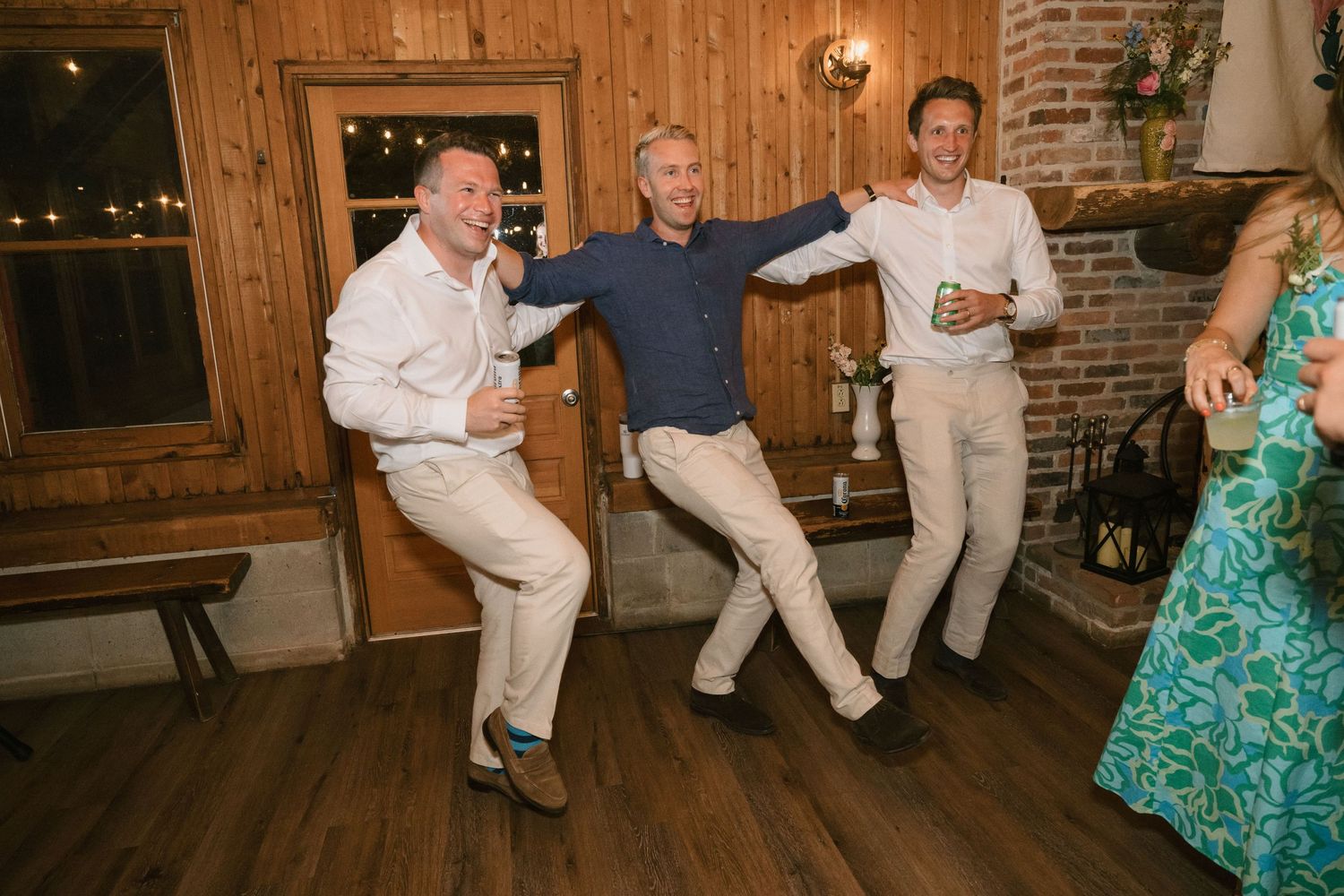 Men in light colored suits dance energetically at a wedding reception.