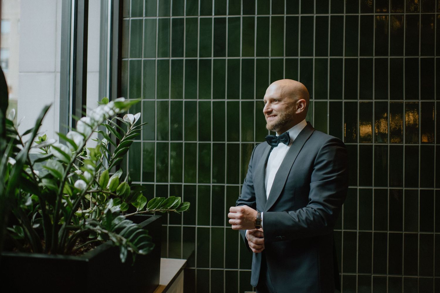 Groom in classic black tuxedo adjusts cufflinks in an elegant setting.