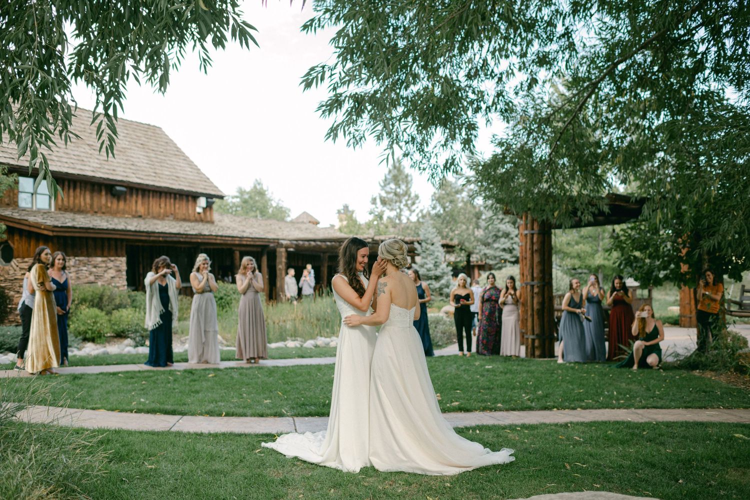 Wedding celebration in a garden setting with guests watching two people in white dresses.