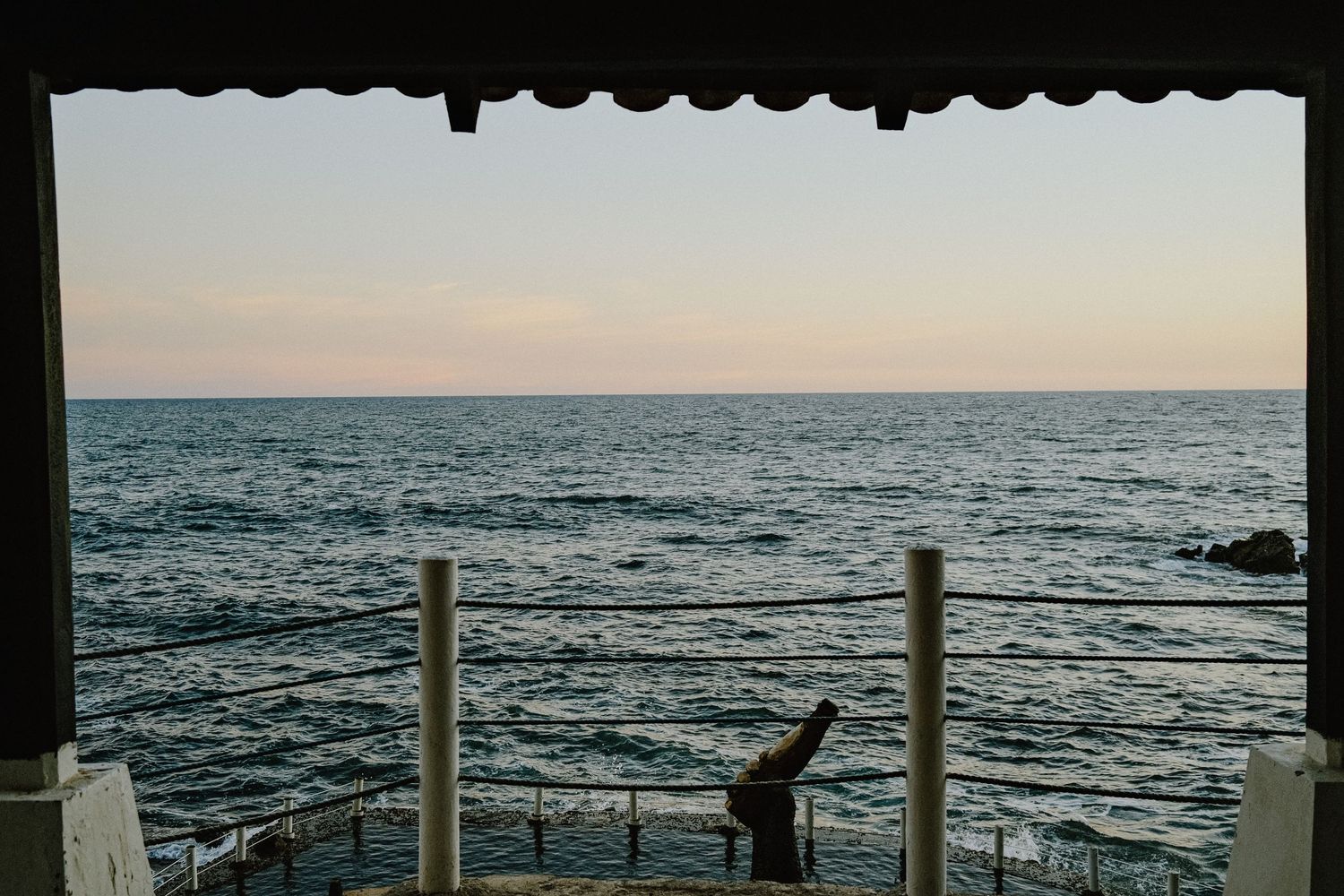 View of ocean horizon and sculptural post through architectural frame at sunset.