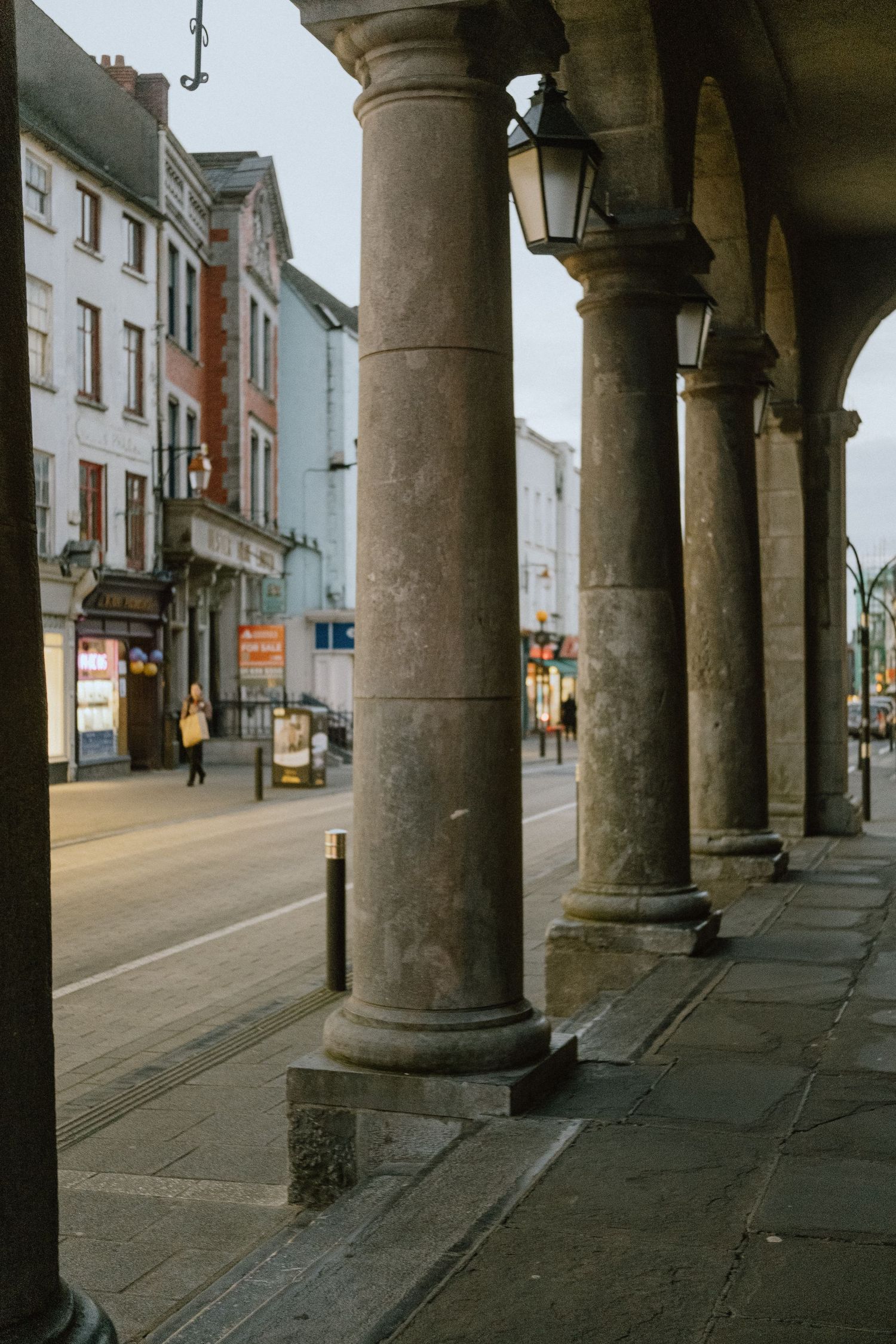 Row of classical stone columns along a city street with traditional architecture.