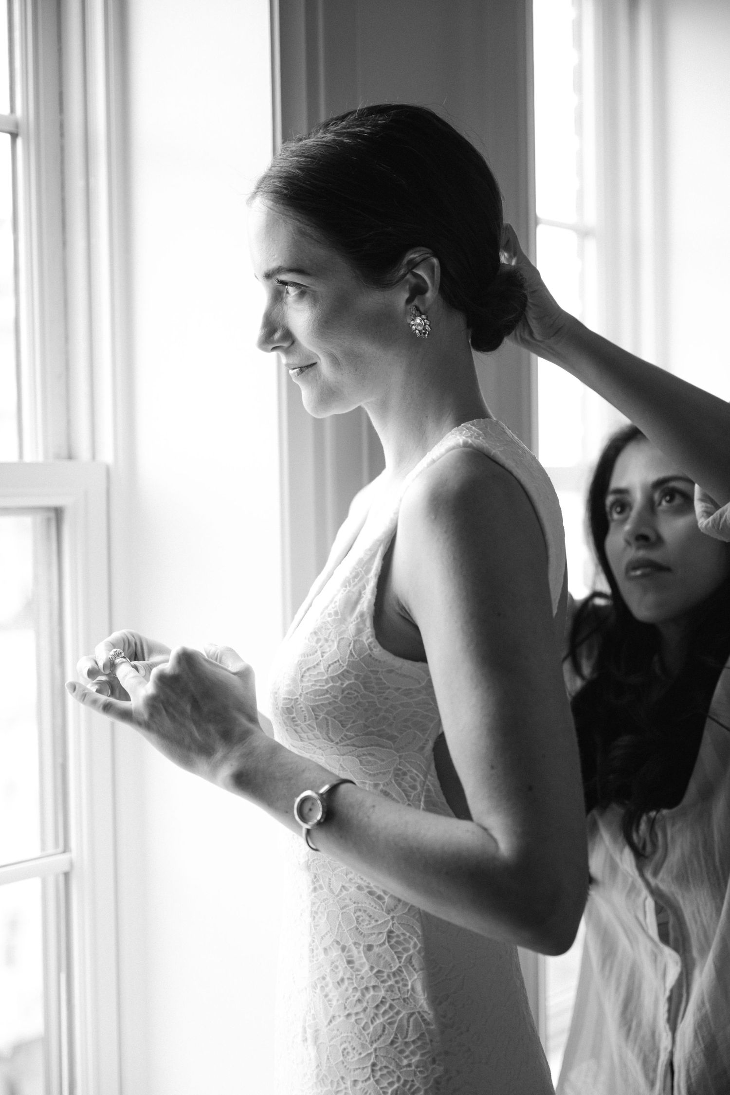 Elegant bride in lace dress gazes out window while getting ready on her wedding day.
