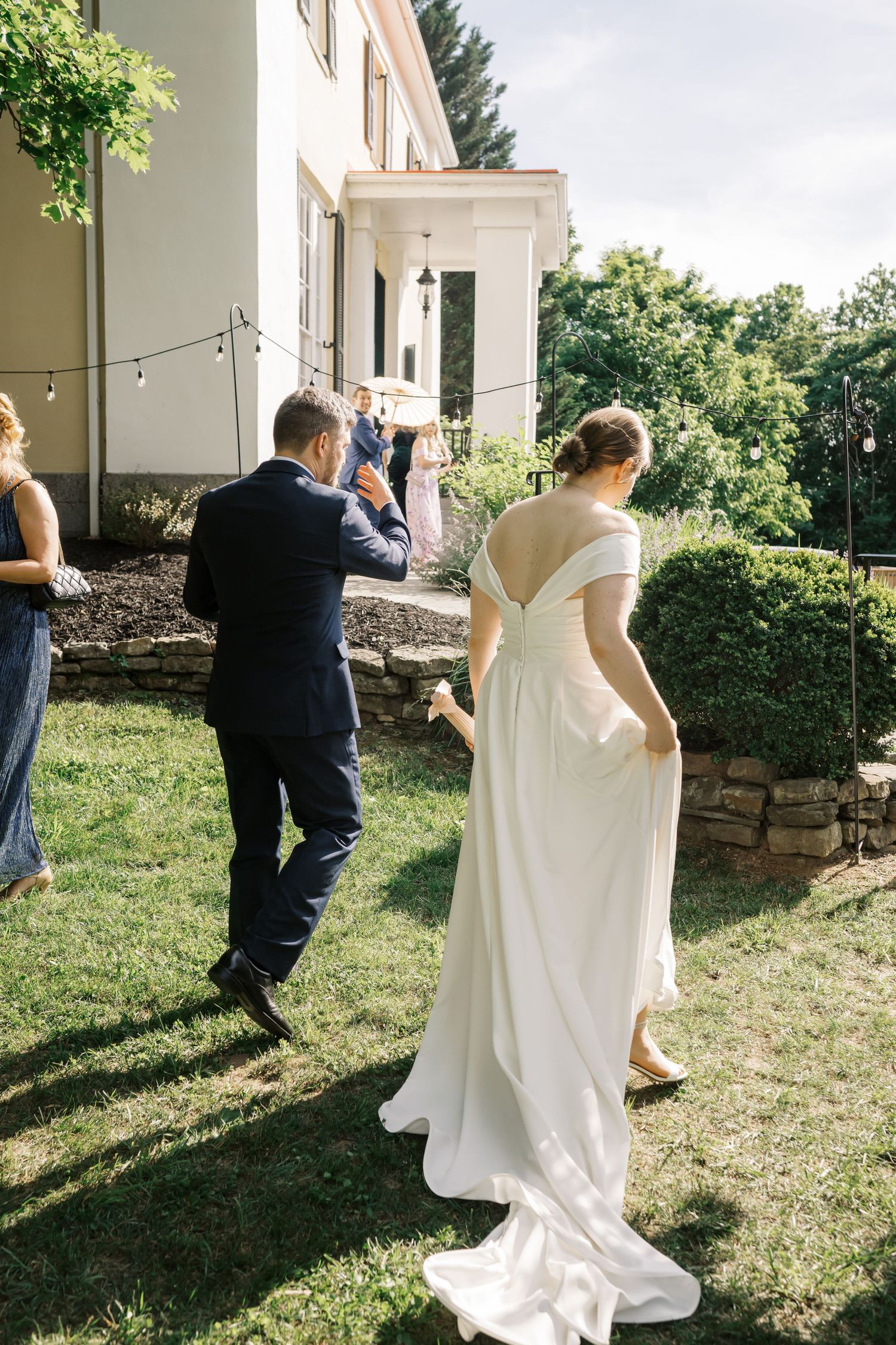 Wedding guests and a bride in a flowing white dress gather outside a stately home.