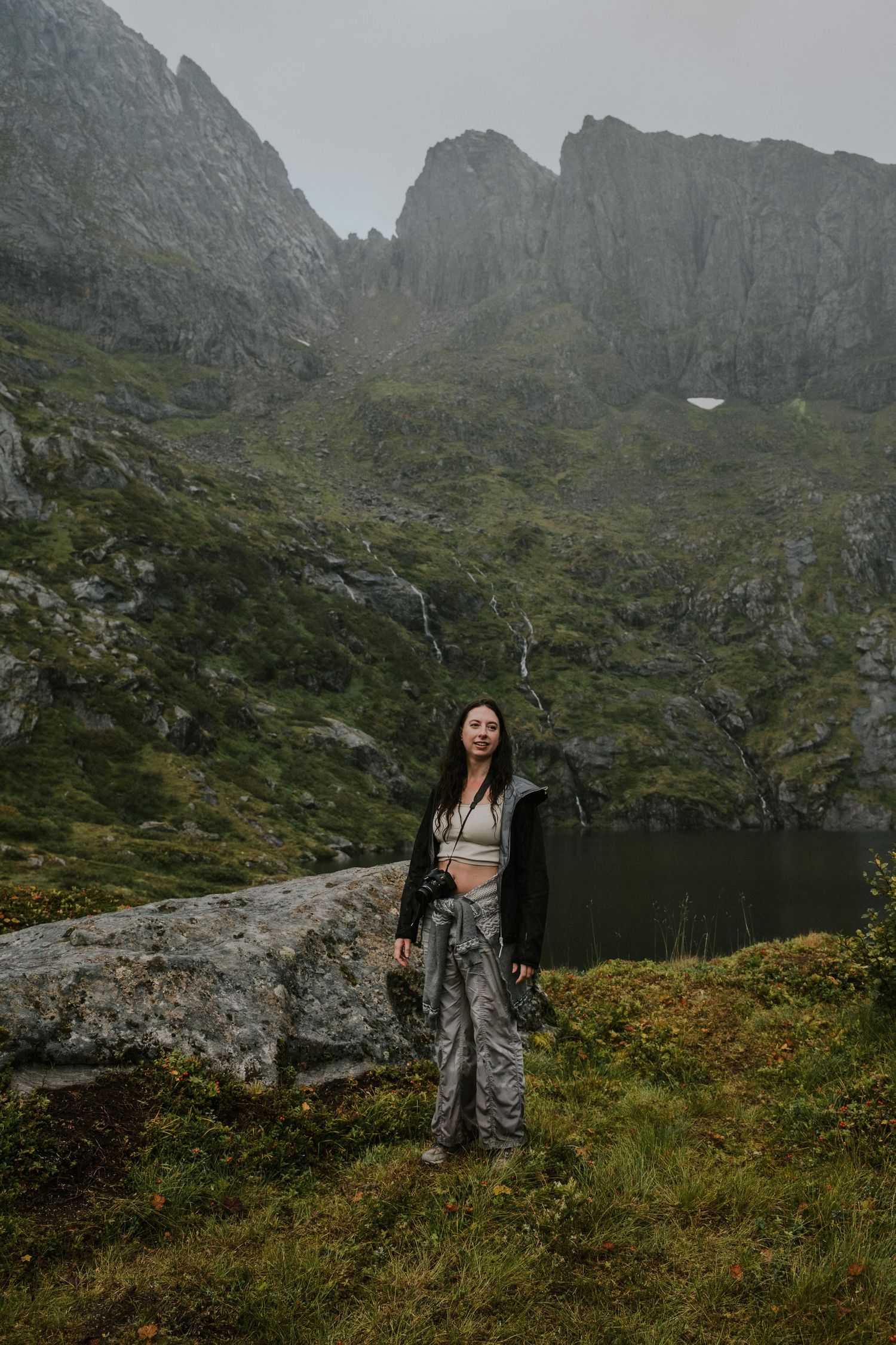 Dramatic mountain landscape with steep cliffs and alpine lake in moody weather conditions.