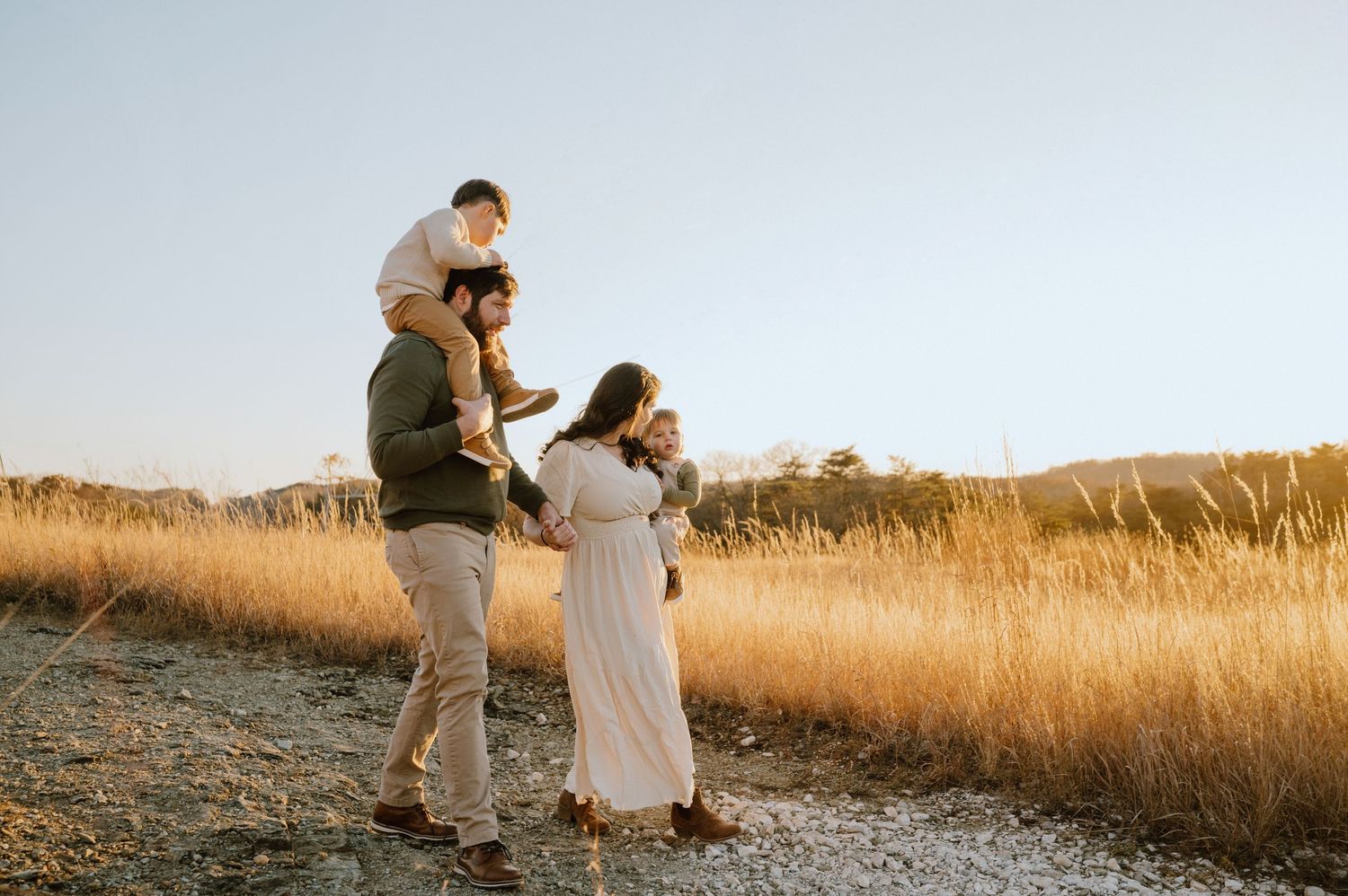 A family walks together through a sunlit meadow during golden hour.