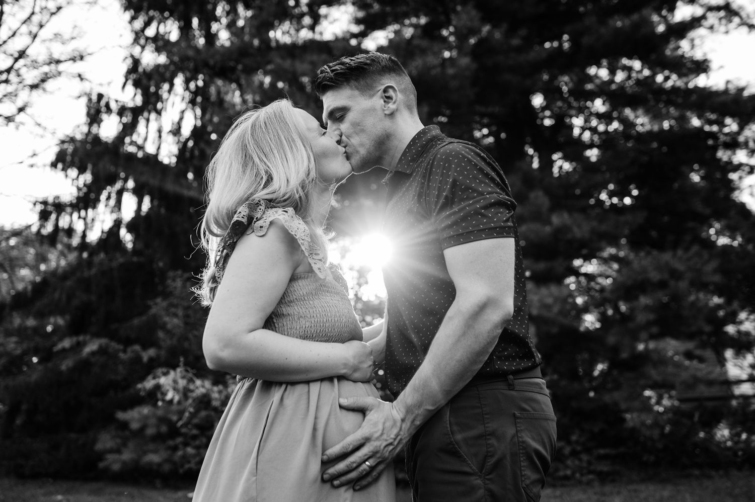 A black and white romantic moment captured with sunlight streaming through pine trees.