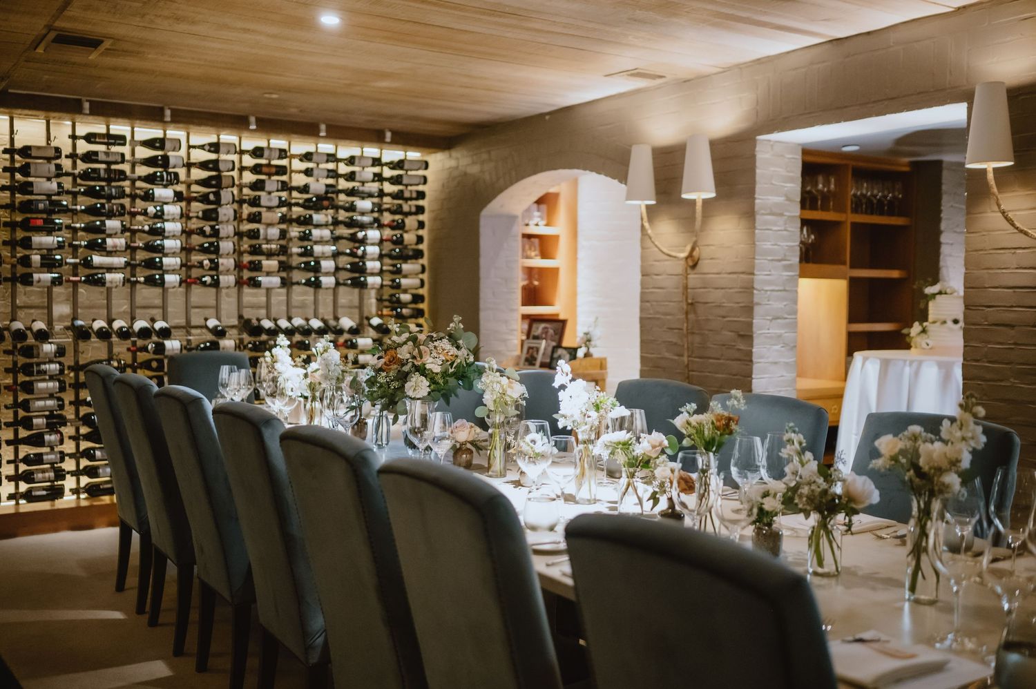 Elegant dining room setup with wine wall display and long table decorated with floral centerpieces.
