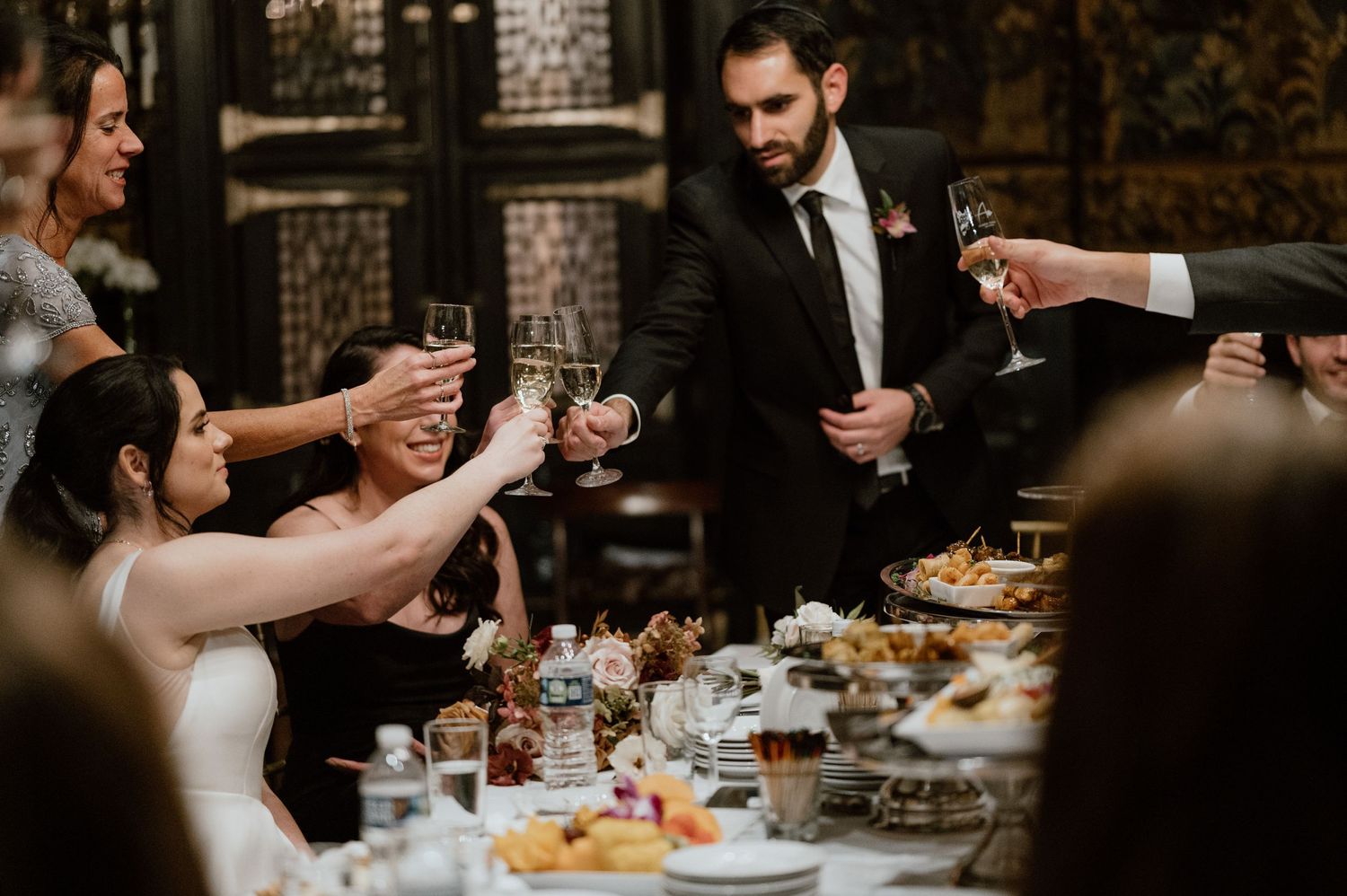 Wedding guests raising glasses during a dinner toast at an elegantly set reception table.