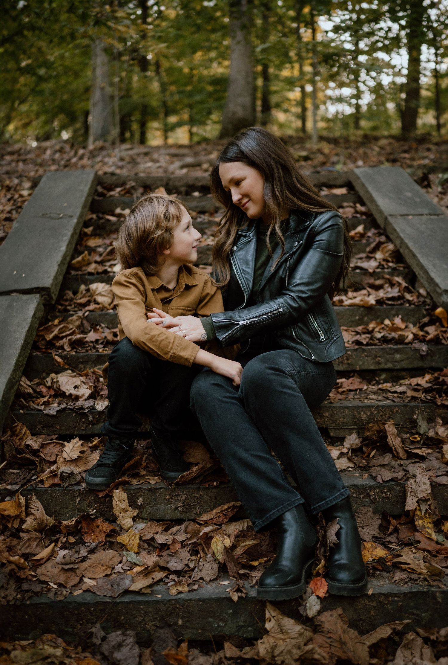 Two people share a tender moment while sitting on rustic wooden steps covered in fall leaves.