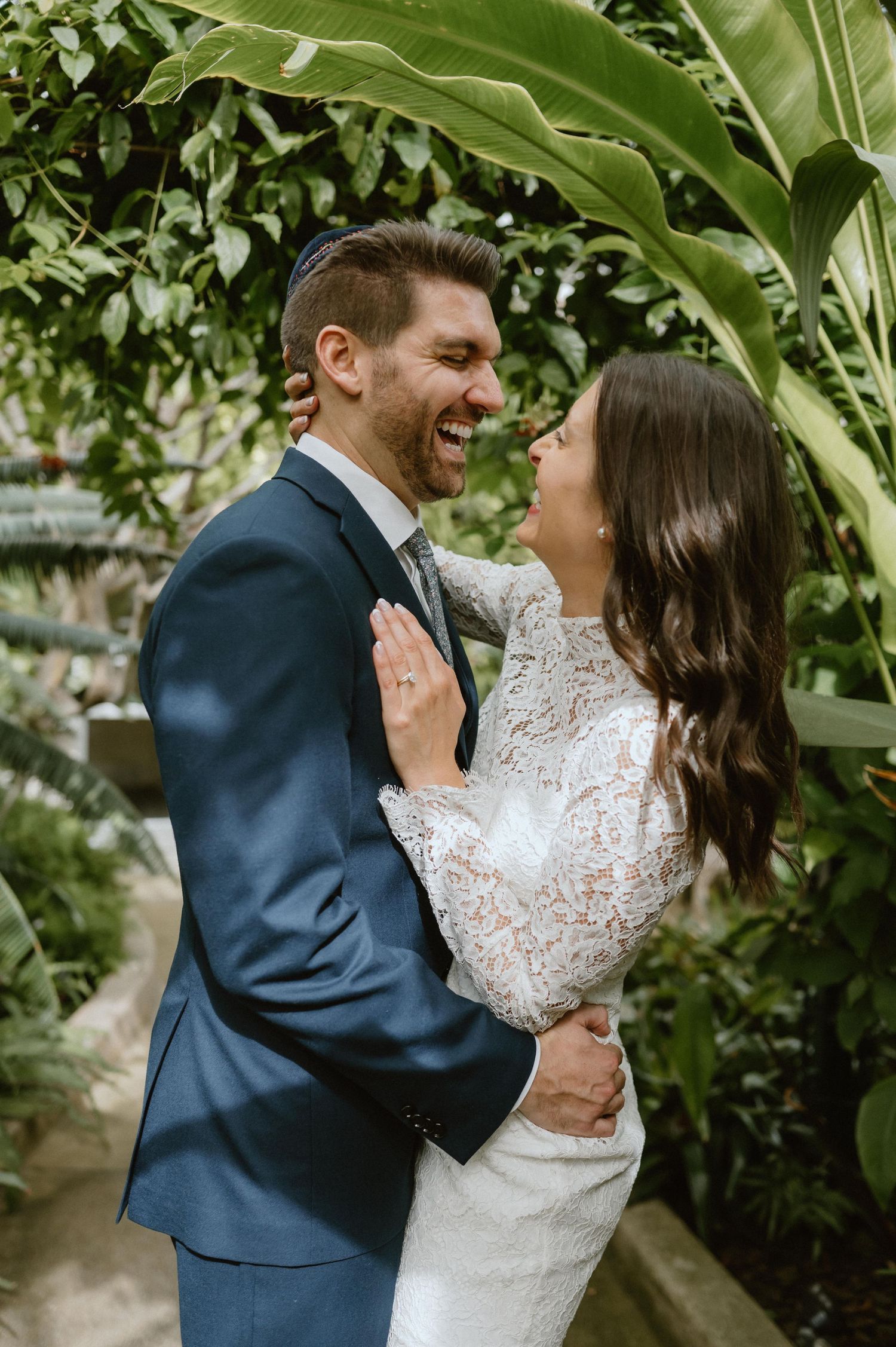 Intimate moment between newlyweds laughing together among tropical plants.